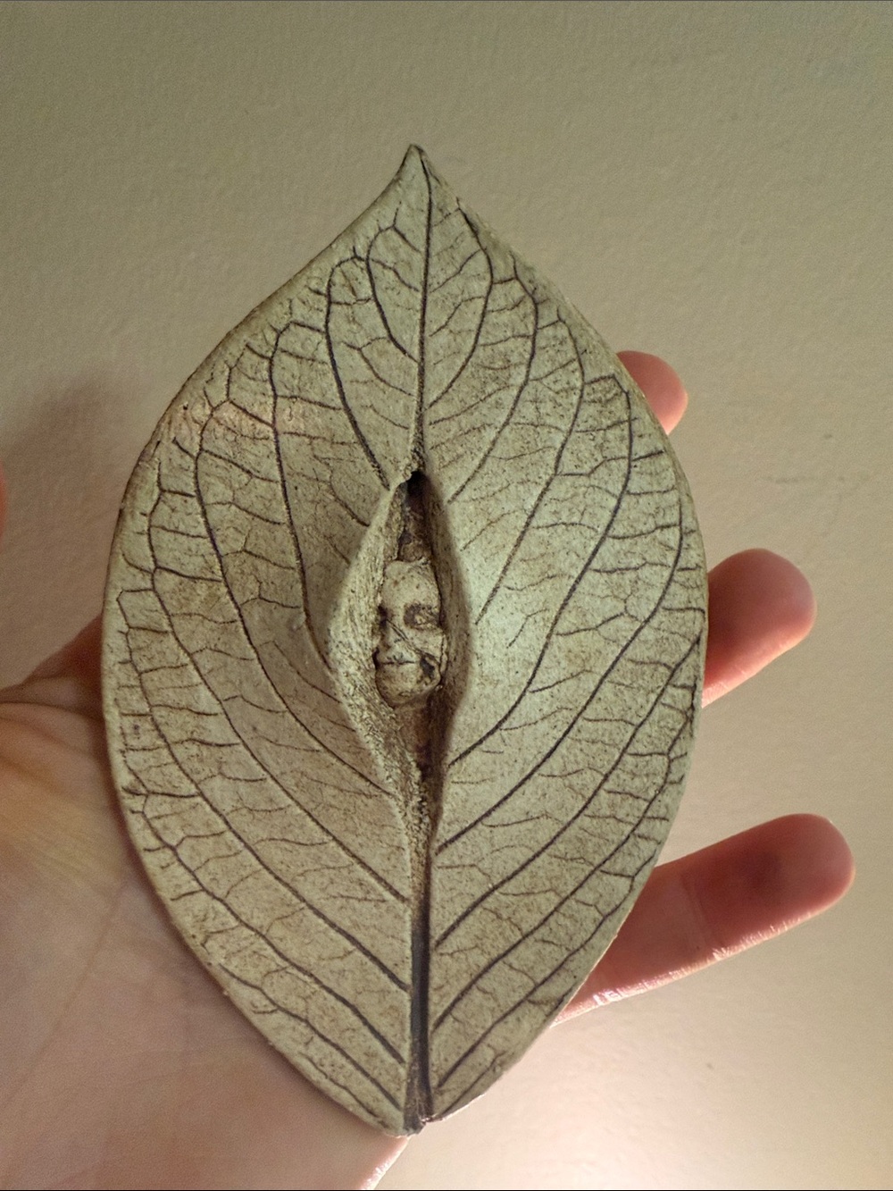 handmade ceramic leaf wall plaque featuring a small sculpted face peeking throug